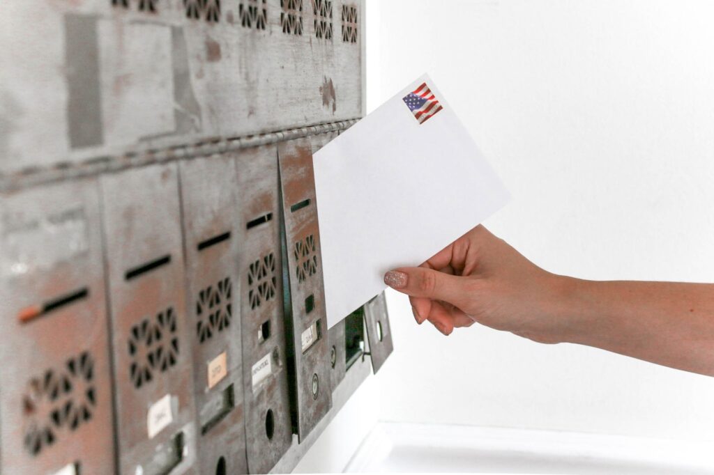 close-up of a hand inserting a stamped envelope into a mailbox, symbolizing voting.