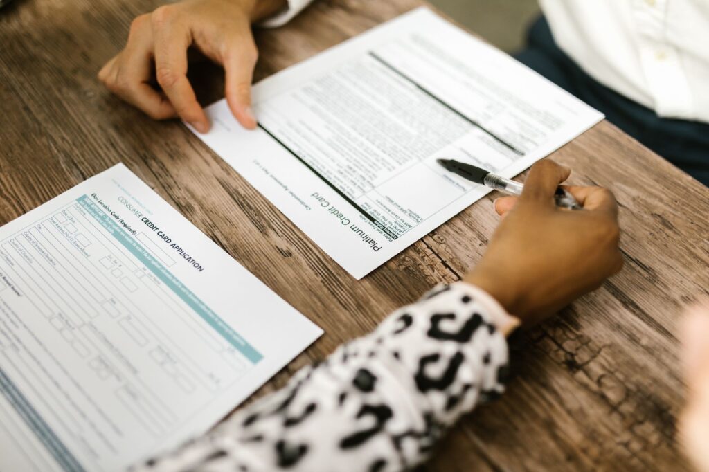 close-up of two people reviewing and filling out a credit card application on a wooden table.