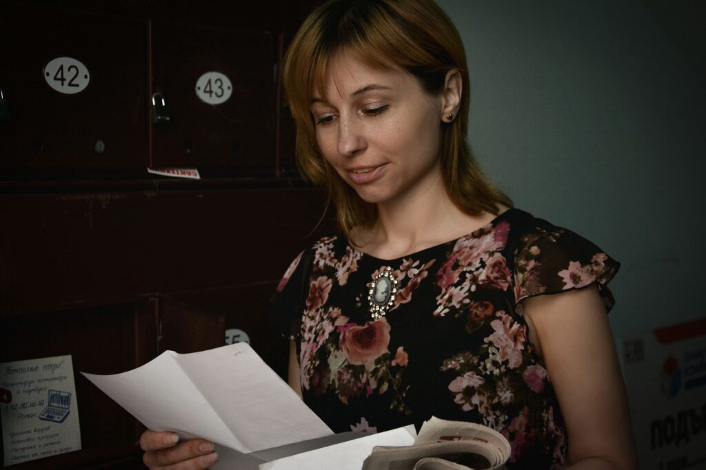 woman reading mail from mailbox in a floral blouse. indoor setting.