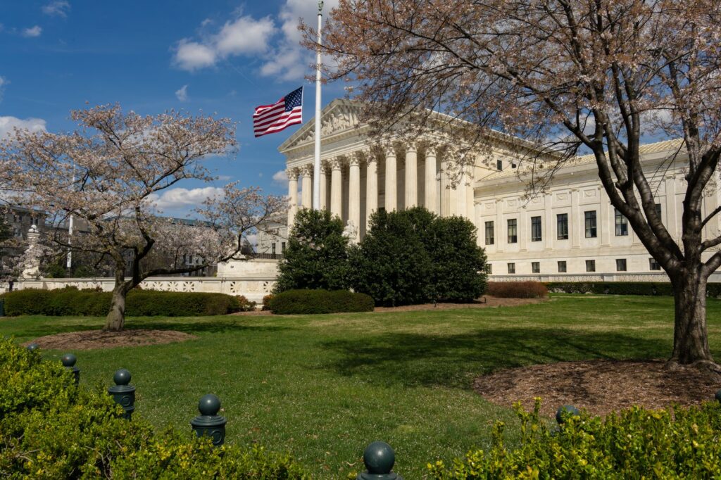 a view of a neoclassical government building with an american flag and cherry blossoms in washington, dc.