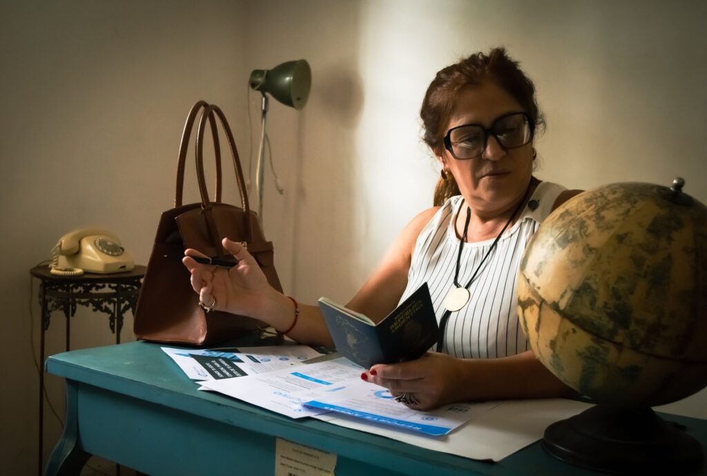woman at a desk reading a passport with a globe and office items nearby, suggesting planning or study.