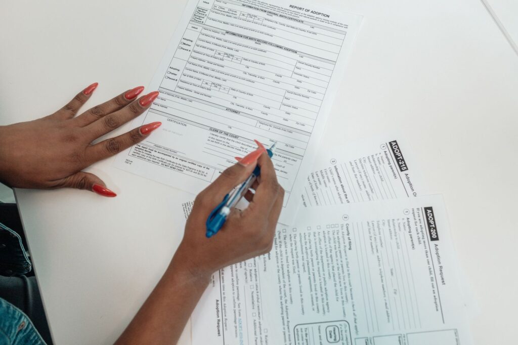 a woman with red nails fills out adoption application forms on a desk.