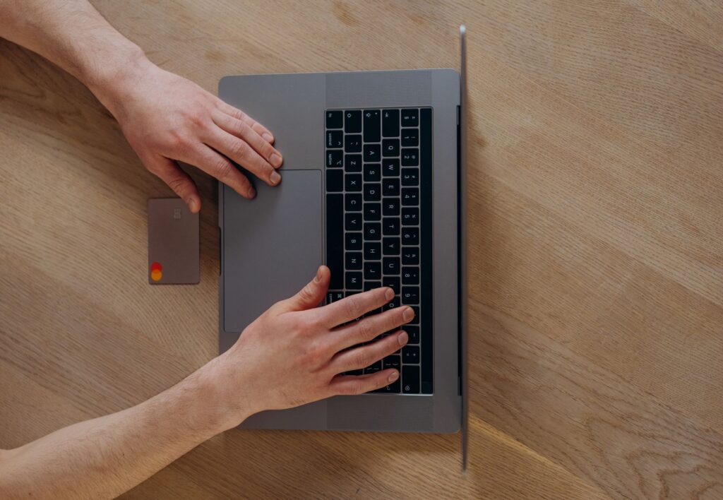a person using a laptop and credit card for online shopping, viewed from above on a wooden table.