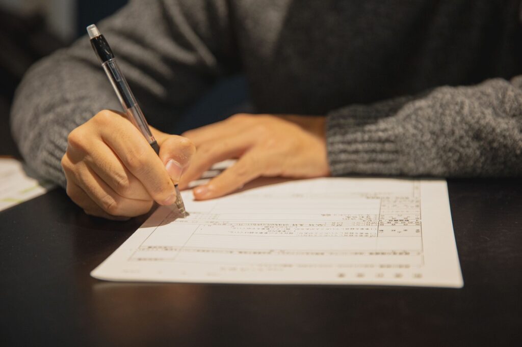 crop anonymous male in gray sweater writing in form of important document at table