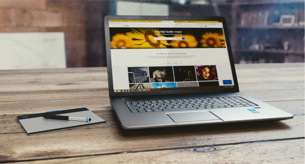 laptop with open webpage on wooden desk, accompanied by tablet and pen, representing digital work setup.
