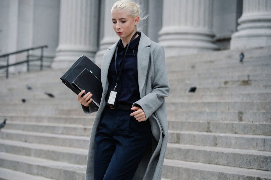 young stylish female lawyer in formal clothes with name tag holding folders while going downstairs near stone building w