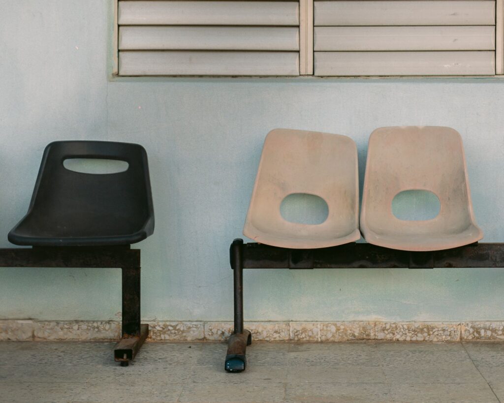 an empty waiting room bench with one black and two beige chairs against a blue wall.