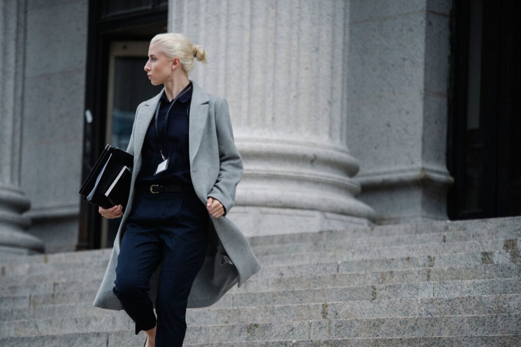 serious female lawyer in elegant outfit holding folders with documents while going downstairs near stone state building