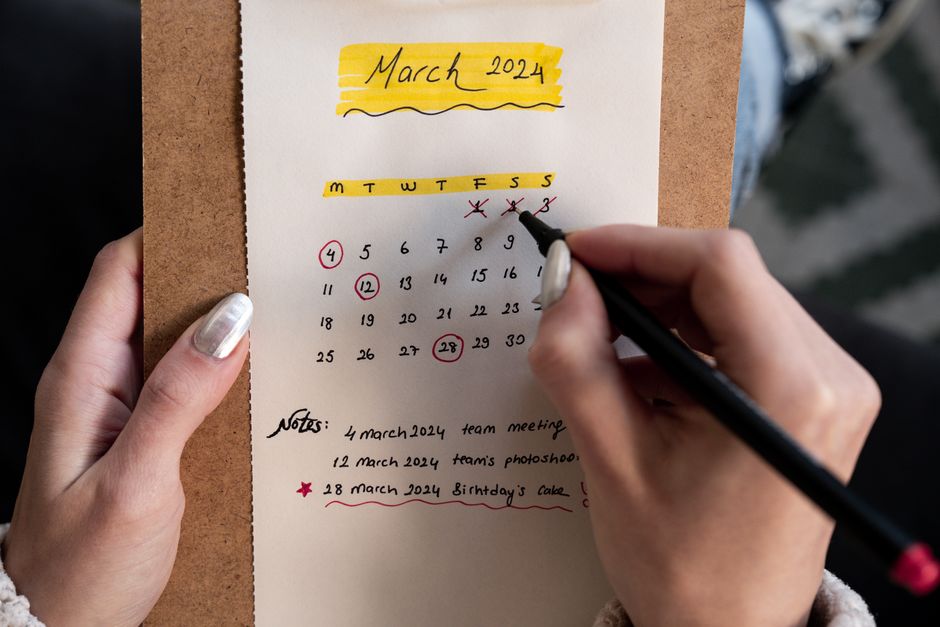 Close-up of a woman's hands organizing a planner for March 2024 with handwritten notes and highlights.