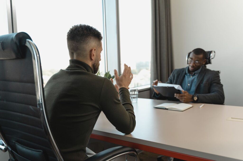 two men in a job interview setting in a modern office with large windows.