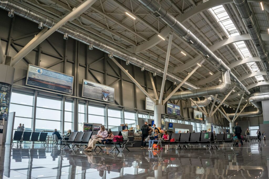 spacious airport terminal interior with passengers seated and walking, showcasing modern design and large windows.