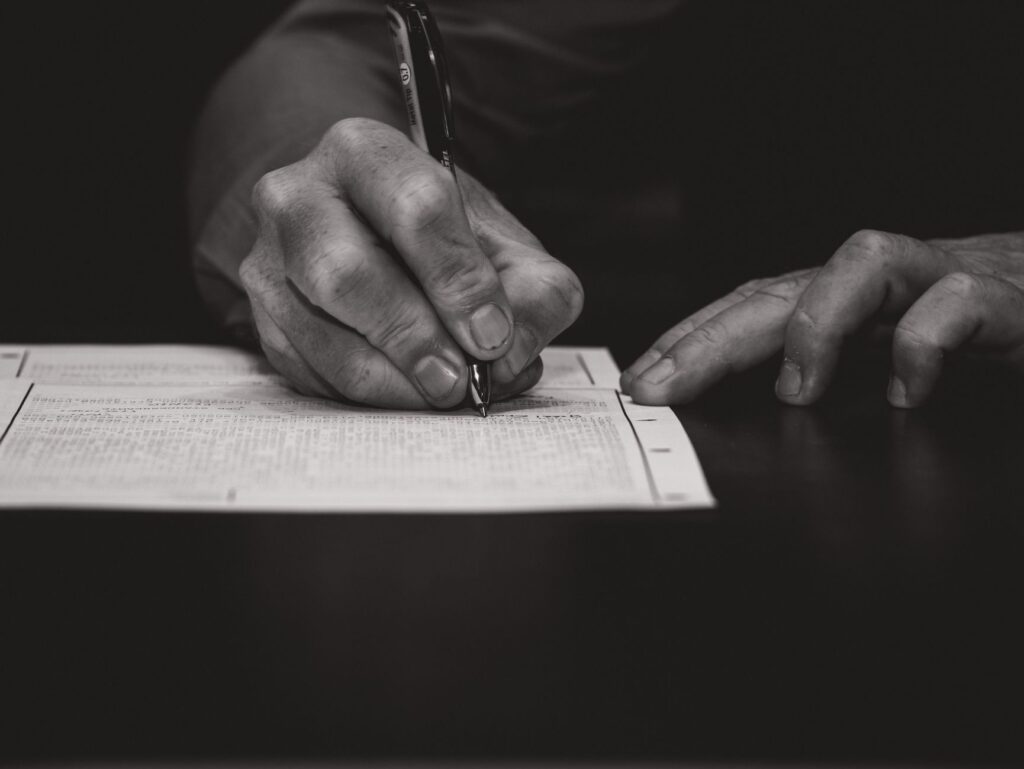 monochrome image of a hand writing on a document, emphasizing attention to detail.