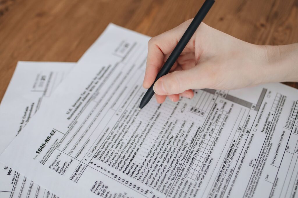 close-up of a hand writing on tax documents with a black pen.