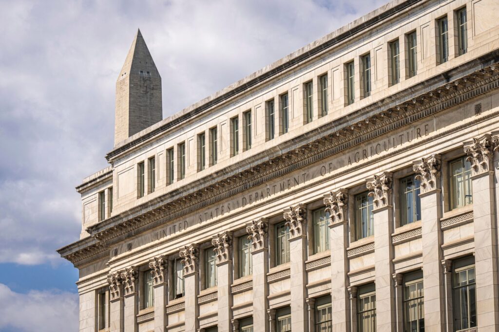 us department of agriculture building with washington monument behind, blue sky with clouds.