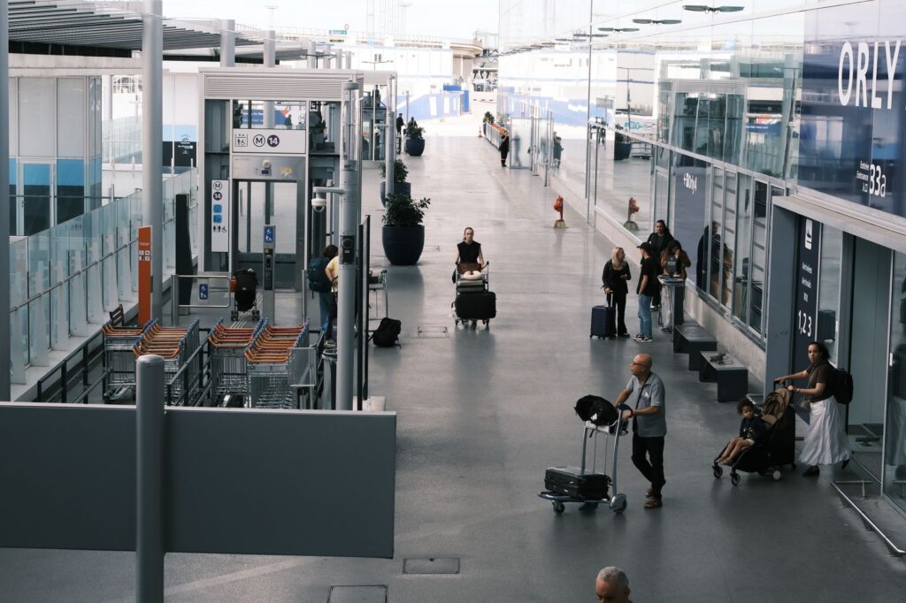 travelers navigate an airport terminal corridor with luggage carts and suitcases.