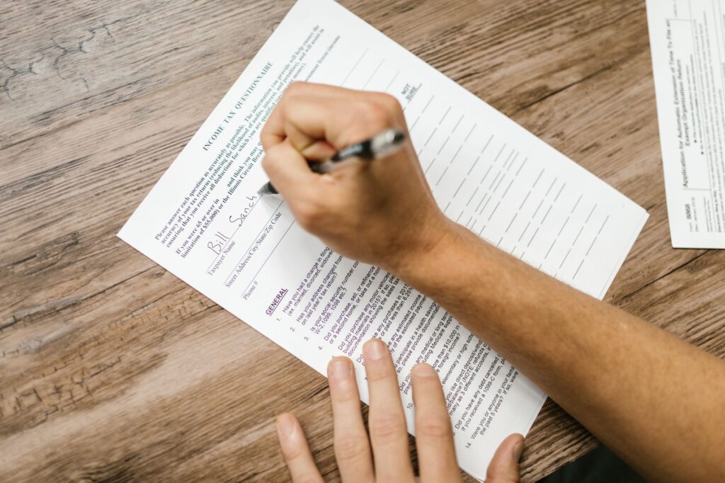 person filling out a tax questionnaire with a pen, showing close-up on wooden table.