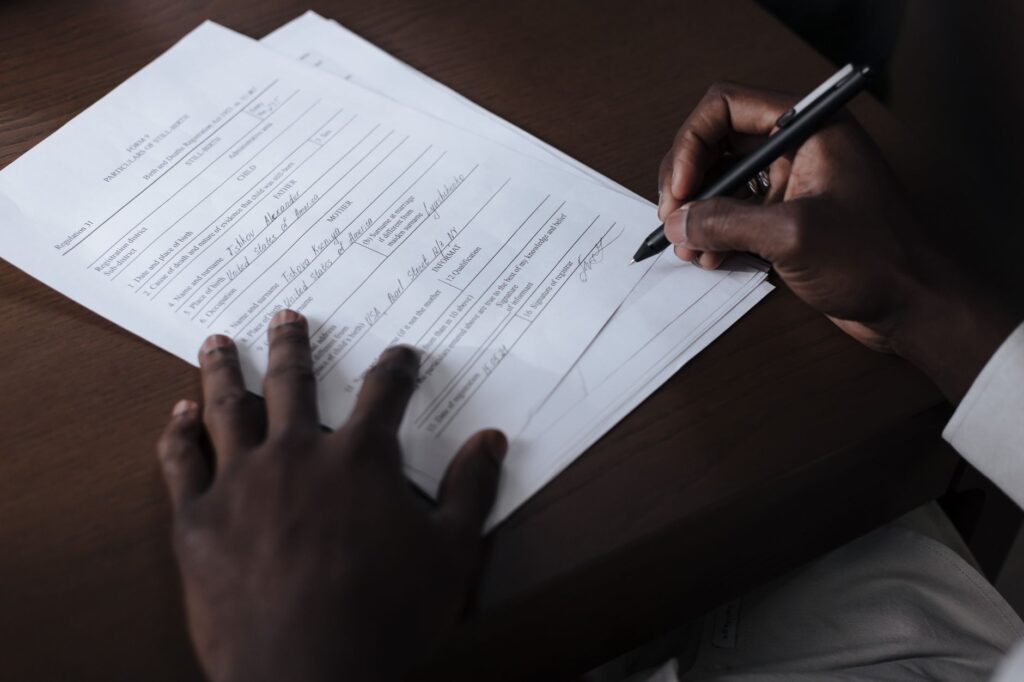 a detailed view of a man signing official documents with a pen at a table.