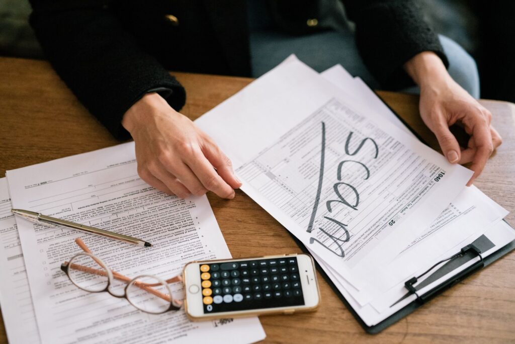 hands of a person examining tax forms labeled as scam with calculator and papers.