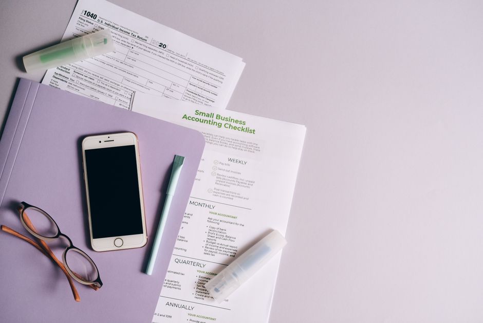 Flat lay of accounting documents, smartphone, and glasses on a desk.