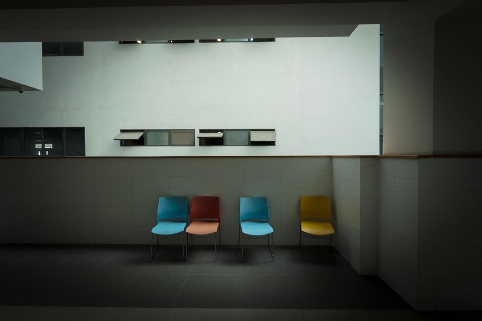 Minimalist interior featuring four colorful chairs against a white wall.