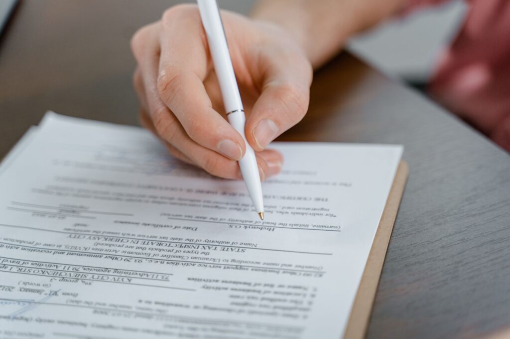 a hand holding a pen signing a document, close-up shot with focus on the paper.