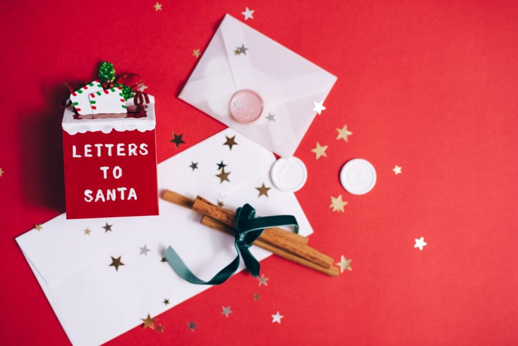a festive flatlay with letters to santa, envelopes, and holiday decorations on a red background.