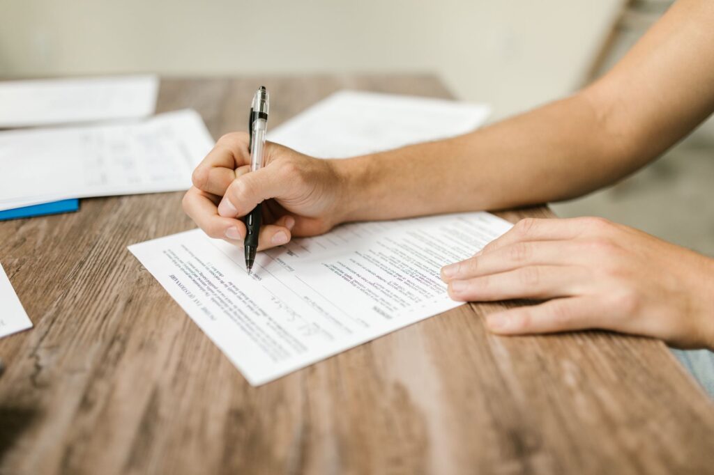 hand filling out paperwork with a pen, showcasing focus on document completion.